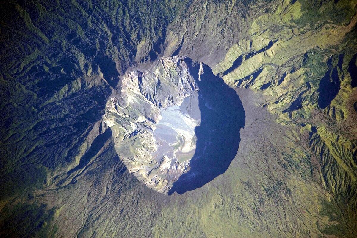 Fotografia de astronauta da caldeira circular no cume do monte Tambora, com paredes internas íngremes e fundo claro