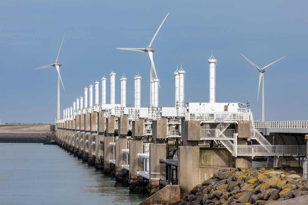 Fila di piloni in cemento e torri delle paratoie d'acciaio della barriera antimareggiata della Schelda orientale, con turbine eoliche sullo sfondo