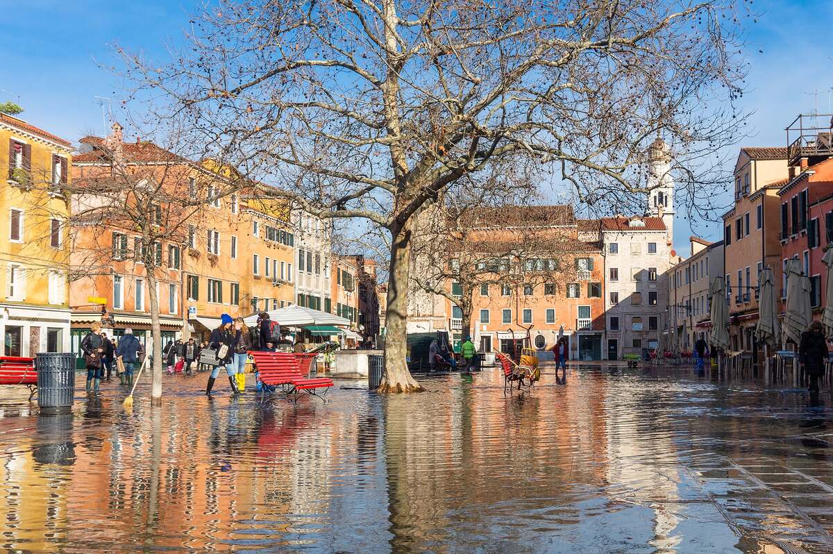 Persone con gli stivali di gomma che attraversano un campo allagato a Venezia, con gli edifici riflessi nell'acqua